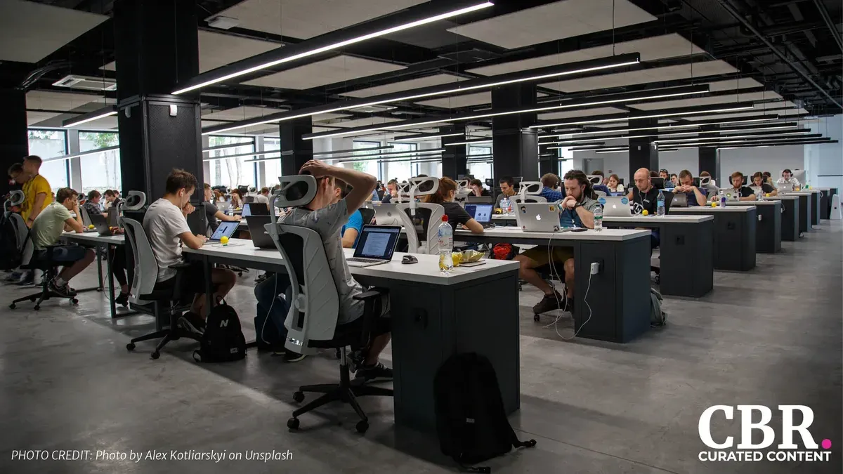 Rows of employees working at laptops at long shared desks in a busy open-plan office