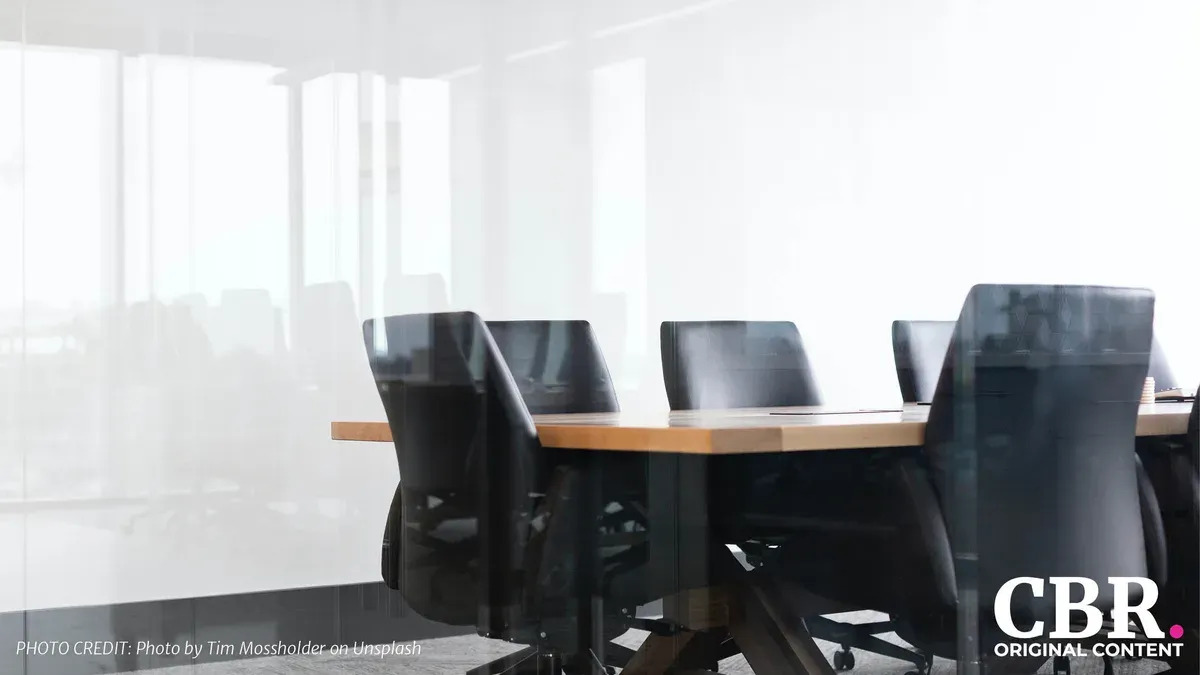 An empty glass-walled boardroom with a row of black office chairs