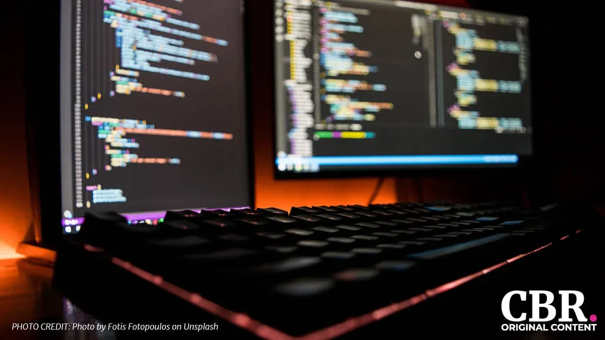 A blurred dual-monitor coding setup behind a mechanical keyboard, lit in orange