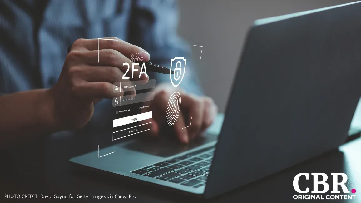 A hand entering login credentials into a two-factor authentication overlay in front of a laptop