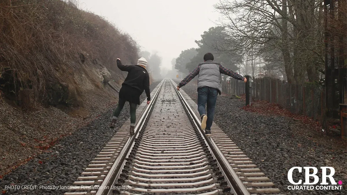 Two people walking away down a foggy railway track with arms outstretched for balance