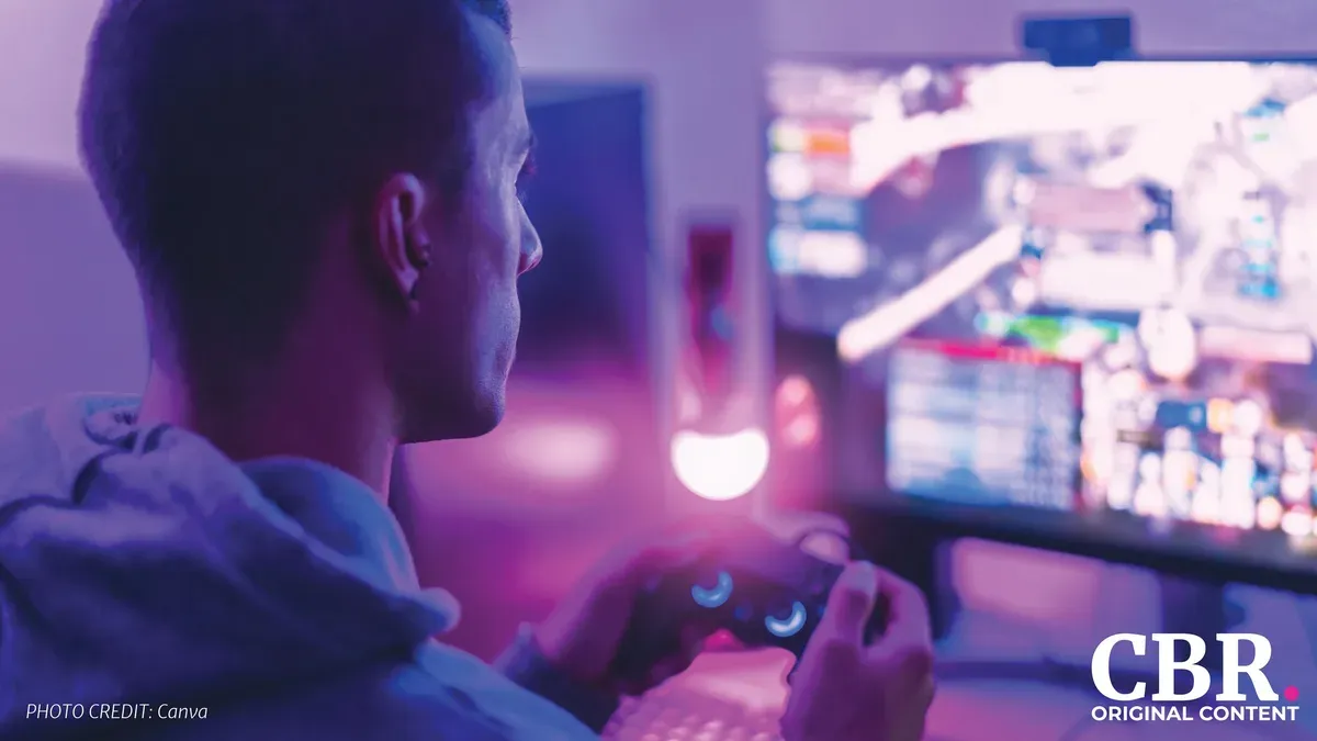 A gamer holding a controller in front of a monitor, lit in purple and pink light