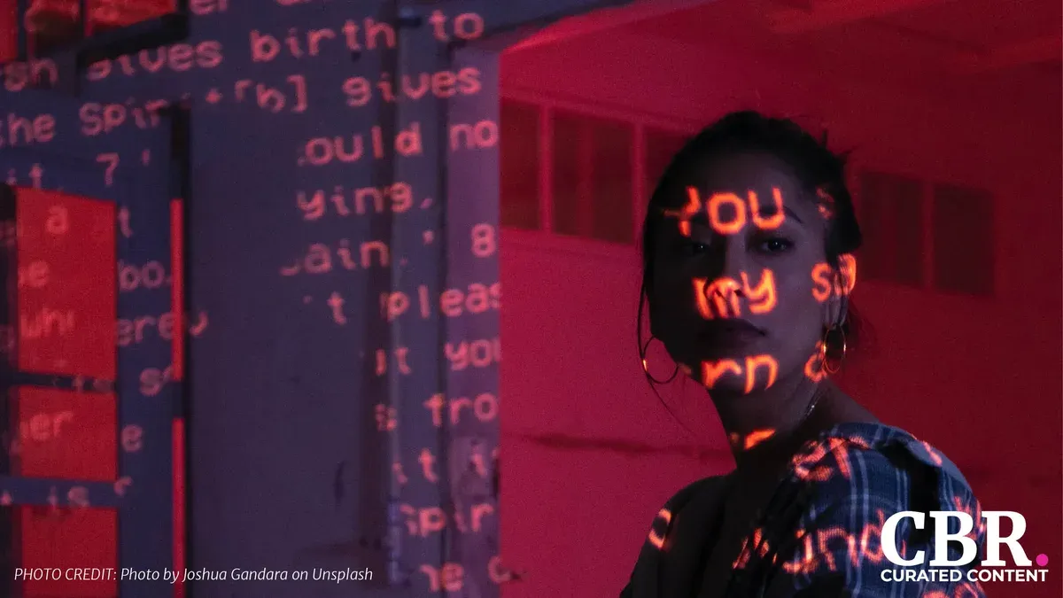A shadowed portrait with glitching red projected text across a person's face and a wall of scrambled text behind them